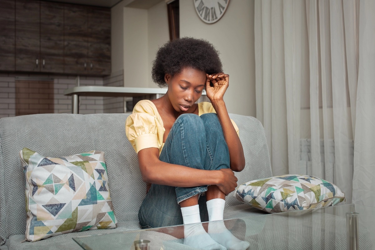 A woman sitting on a couch with her knees to her chest, struggling with withdrawal and considering detox. A woman sitting on a couch with her knees to her chest, struggling with withdrawal and considering detox.