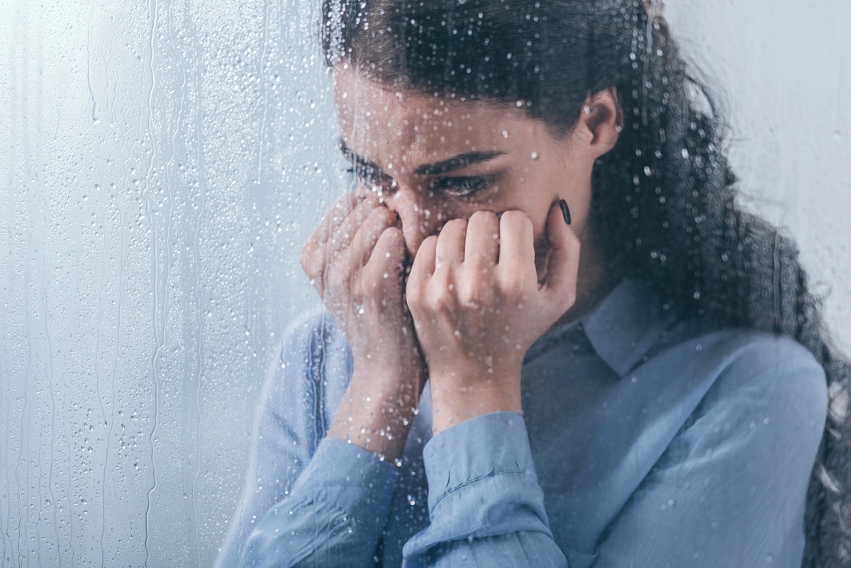 A woman crying behind a glass window, possibly suffering from symptoms of persistent depressive disorder.
