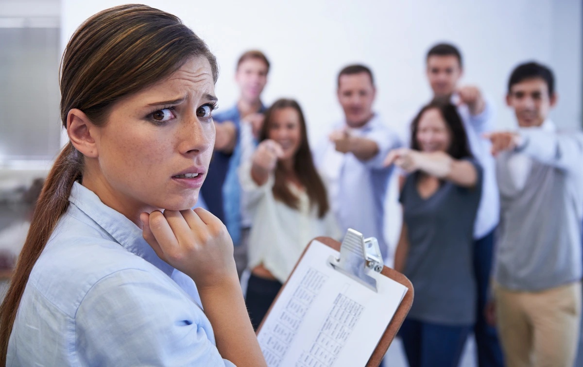 social-anxiety-disorder A woman feeling as if her coworkers are laughing at her, possibly suffering from social anxiety disorder.