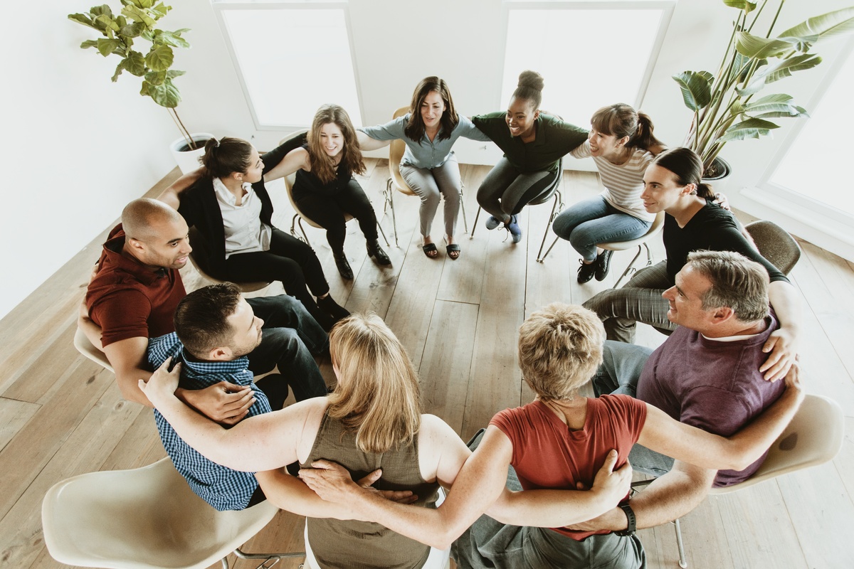 A group therapy session at alcohol rehab, with people placing their arms on their partners' backs. A group therapy session at alcohol rehab, with people placing their arms on their partners' backs.