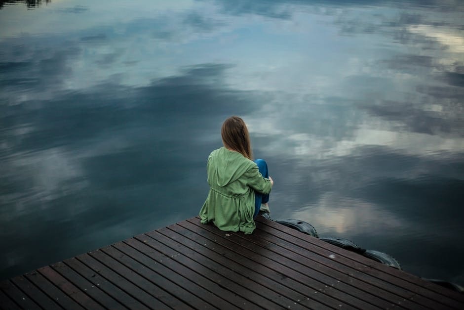 Does Drug Rehab Treat Depression? Photo of a young woman sitting on the edge of a dock in cloudy weather.