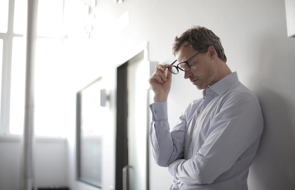 What Are the 5 Most Common Anxiety Disorders?  Photo of a man learning aginst a wall taking his glasses off.