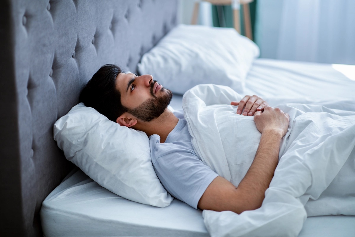 seasonal-affective-disorder A man laying in bed during a gloomy day and possibly suffering from symptoms of seasonal affective disorder (SAD).