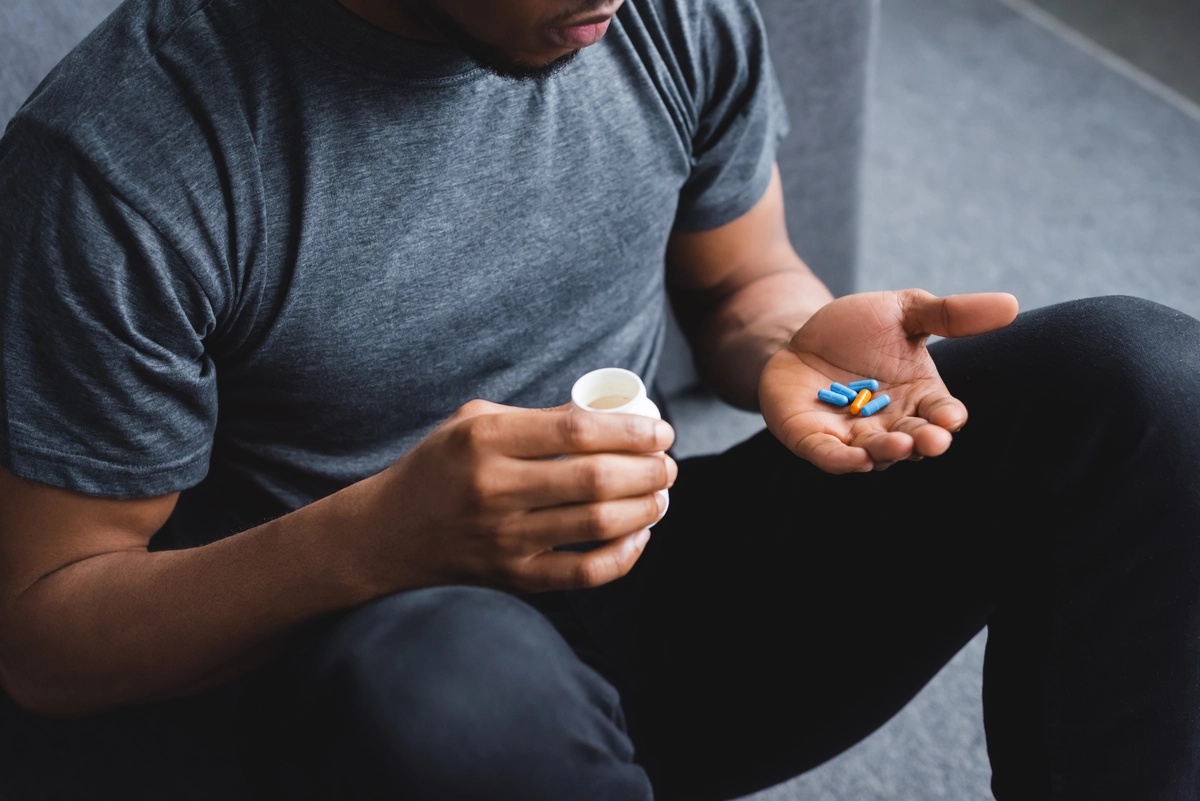 A man sitting down and holding a handful of stimulants in his hand, possibly struggling with stimulant addiction. A man sitting down and holding a handful of stimulants in his hand, possibly struggling with stimulant addiction.