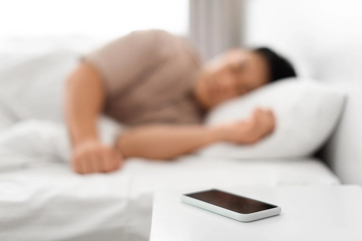 A person sleeping with their phone sitting on the nightstand, possibly suffering from a phone addiction. A person sleeping with their phone sitting on the nightstand, possibly suffering from a phone addiction.