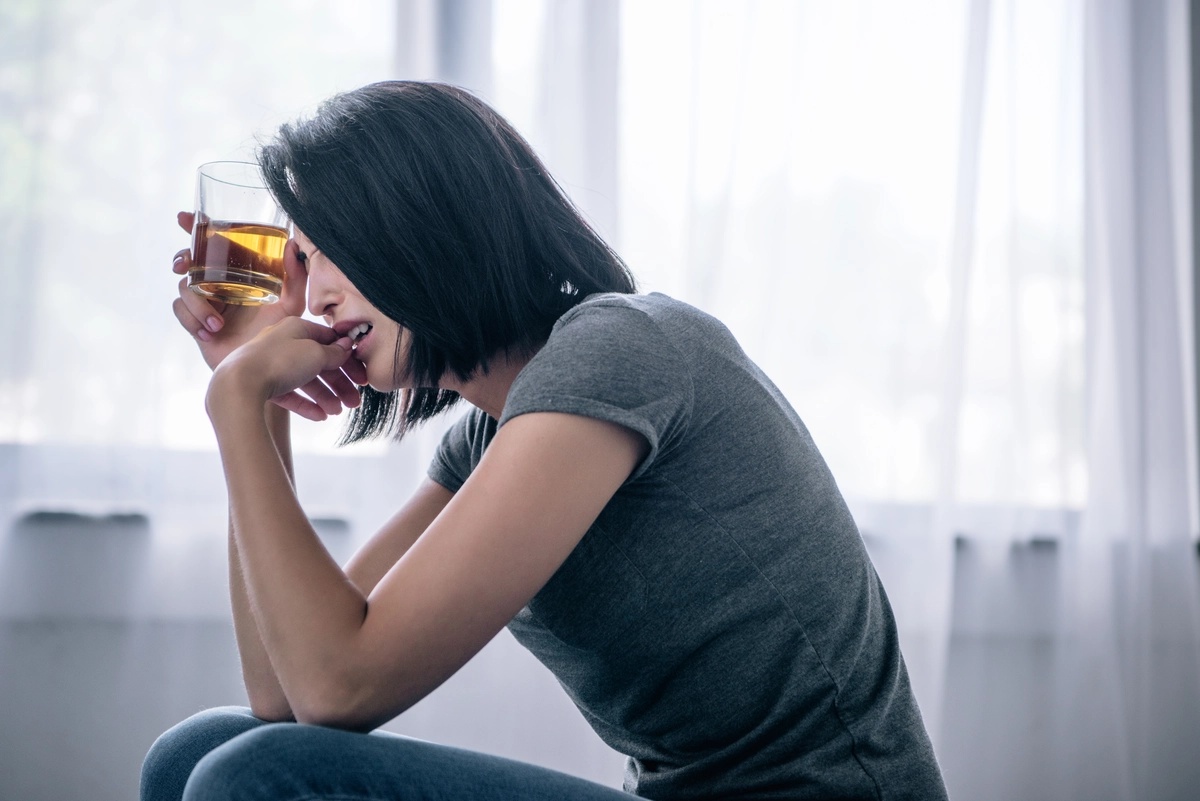 A woman crying as she holds a glass of whiskey to her head, possibly struggling with alcohol addiction. A woman crying as she holds a glass of whiskey to her head, possibly struggling with alcohol addiction.