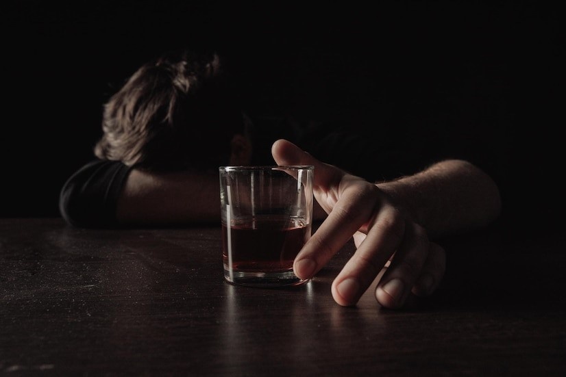 Is Drug and Alcohol Addiction a Disease? Photo of a man with his head down at a bar, a drink near his hand.
