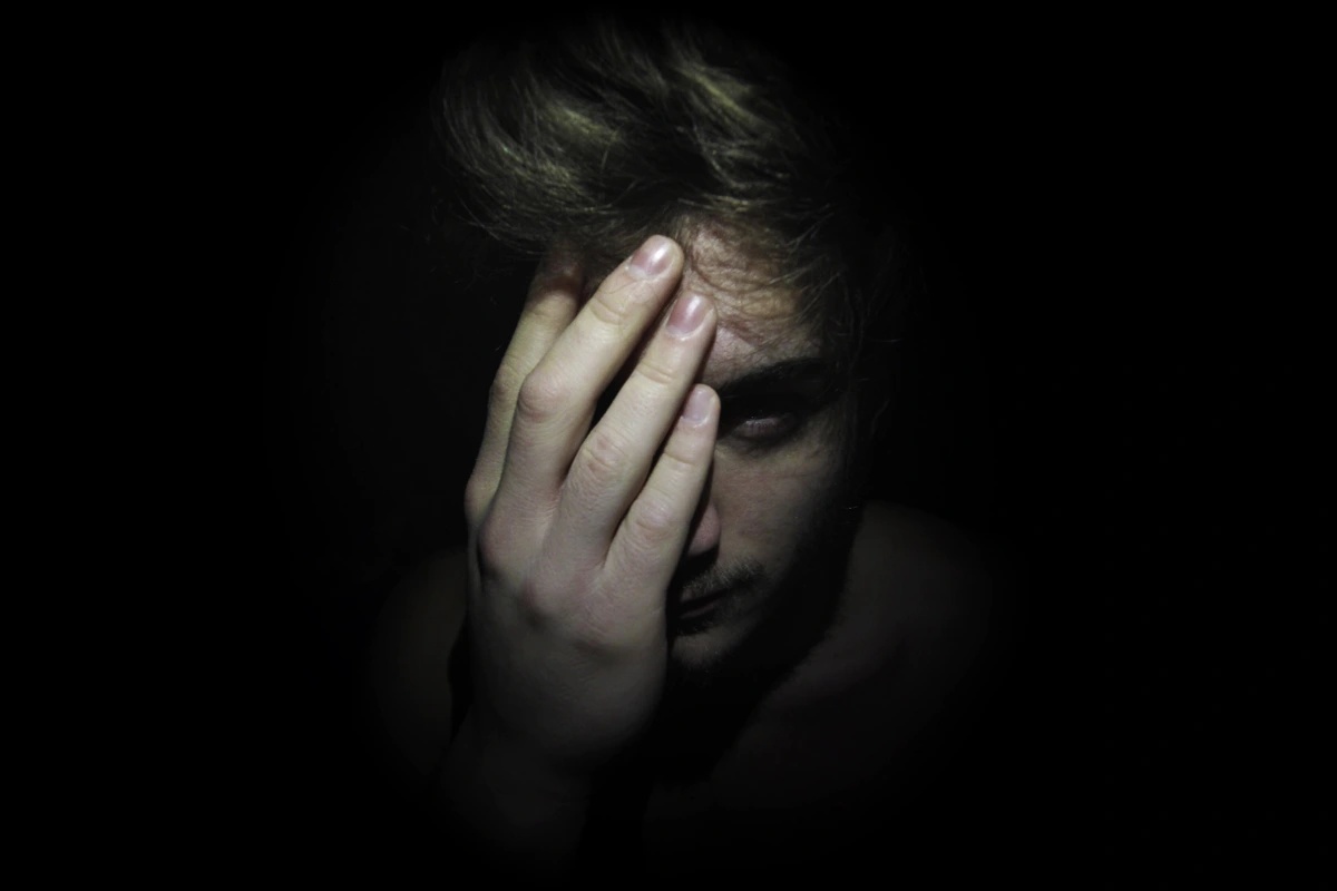 A man suffering from simple schizophrenia in a dark room holding his hand over his eye. A man suffering from simple schizophrenia in a dark room holding his hand over his eye.